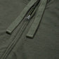Close-up of an olive green zip-up hoodie showing the front zipper, drawstrings, and textured fabric.